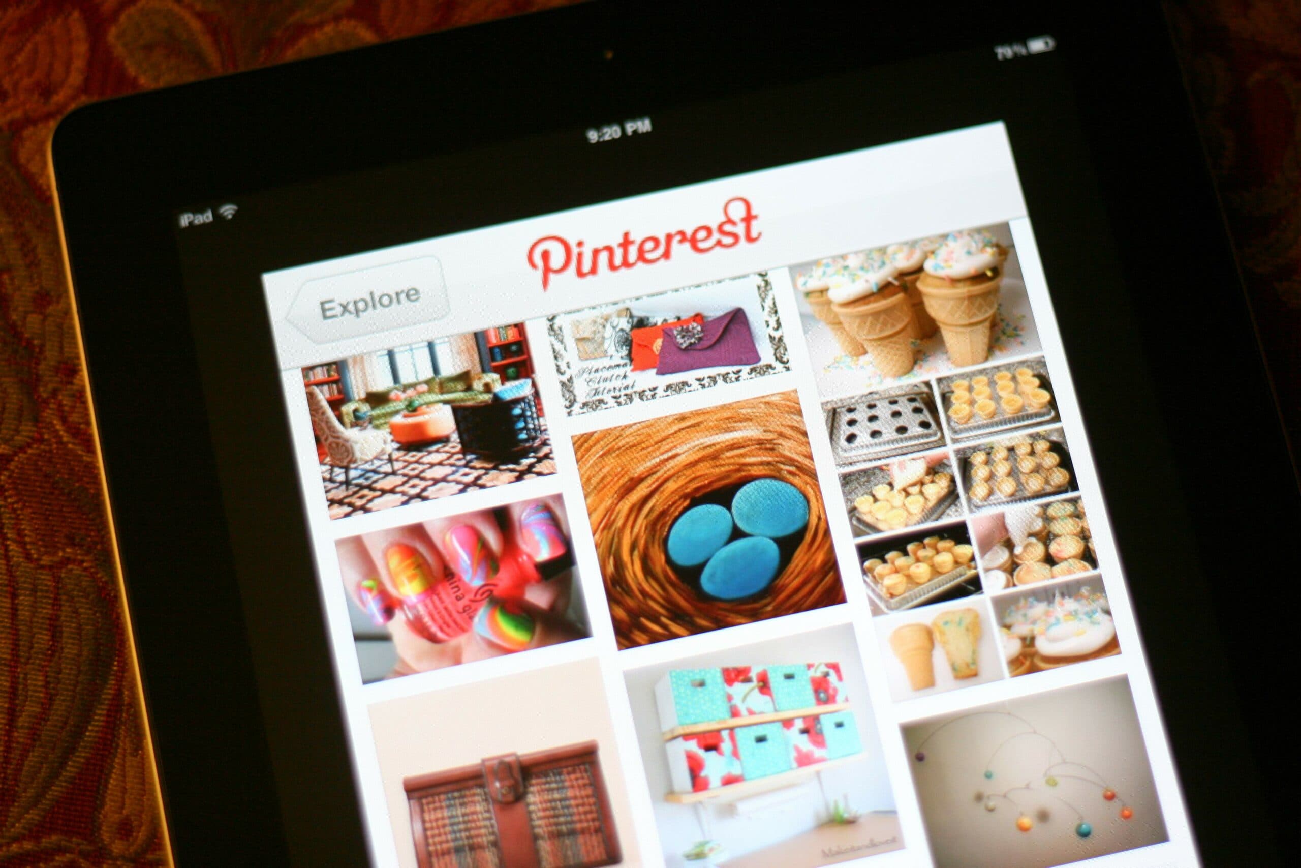 A tablet displaying the Pinterest app interface with a grid of colorful images, including photos of food, crafts, and decor items, on a patterned background.