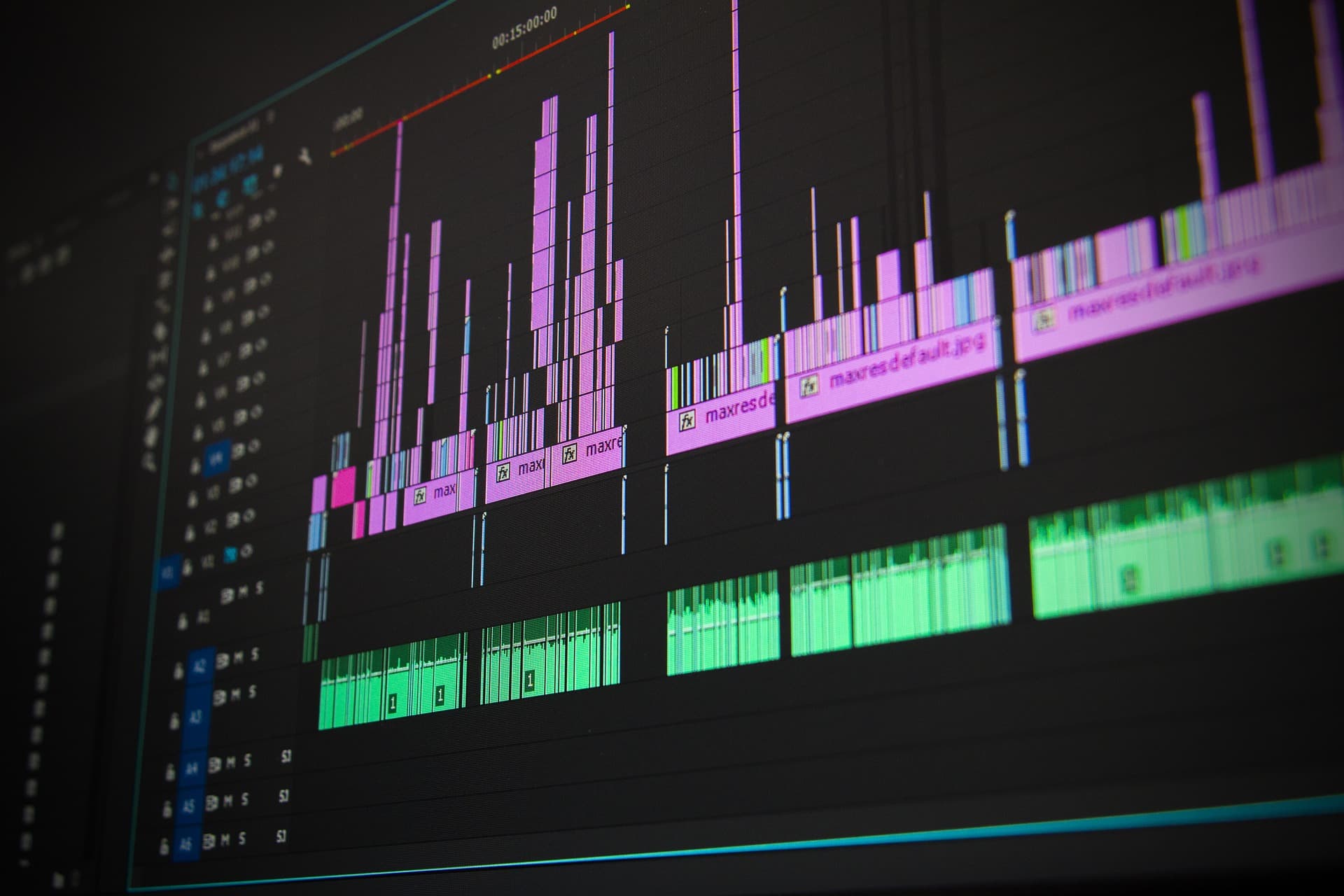 Close-up of a computer screen displaying audio tracks in a digital editing software. The timeline shows a mix of pink and green waveforms with multiple tracks and layers, indicating a complex audio or video editing project.