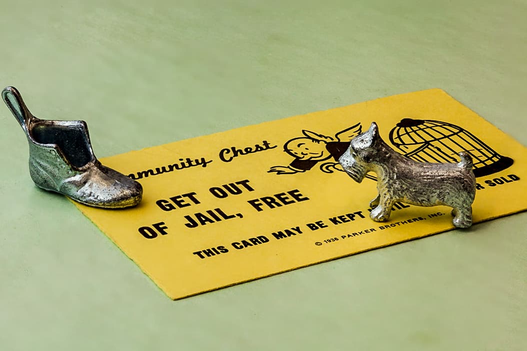 Monopoly game pieces, a shoe and a dog, are placed next to a yellow Get Out of Jail, Free card on a green background.