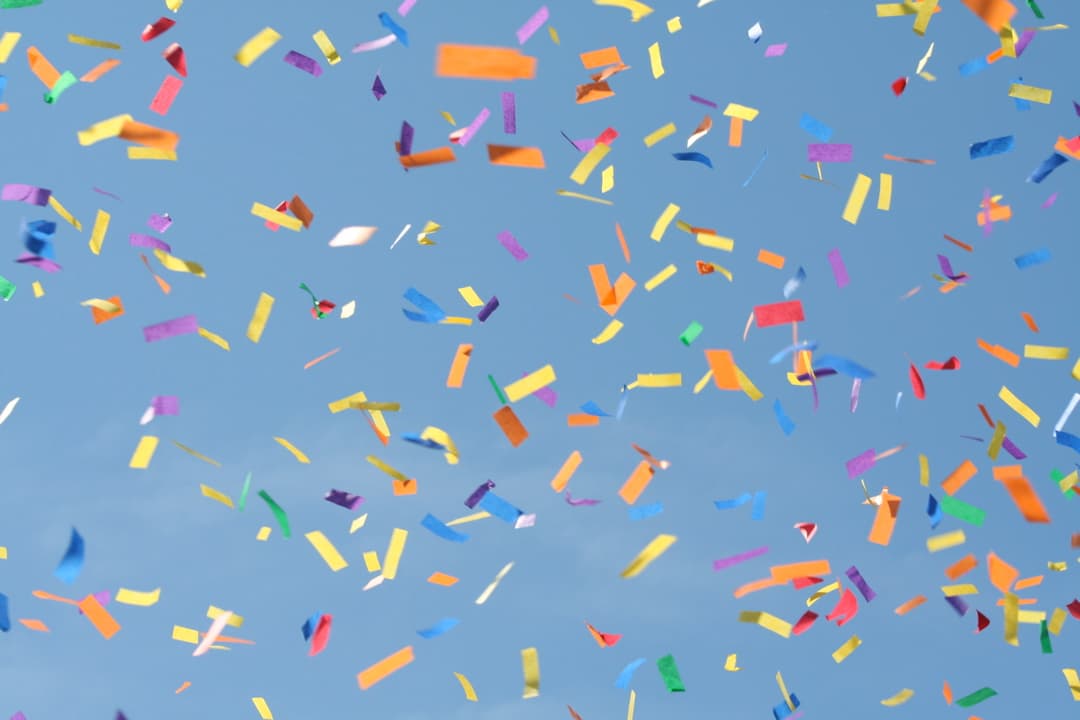 Colorful confetti pieces falling against a clear blue sky.