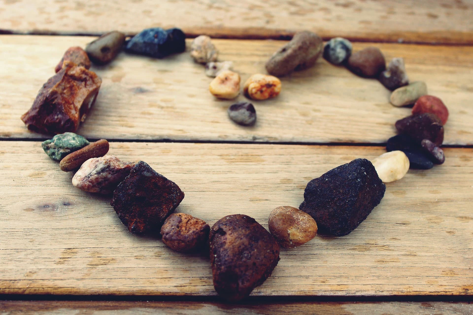 Heart shape made from variously sized and colored stones arranged on a wooden surface.