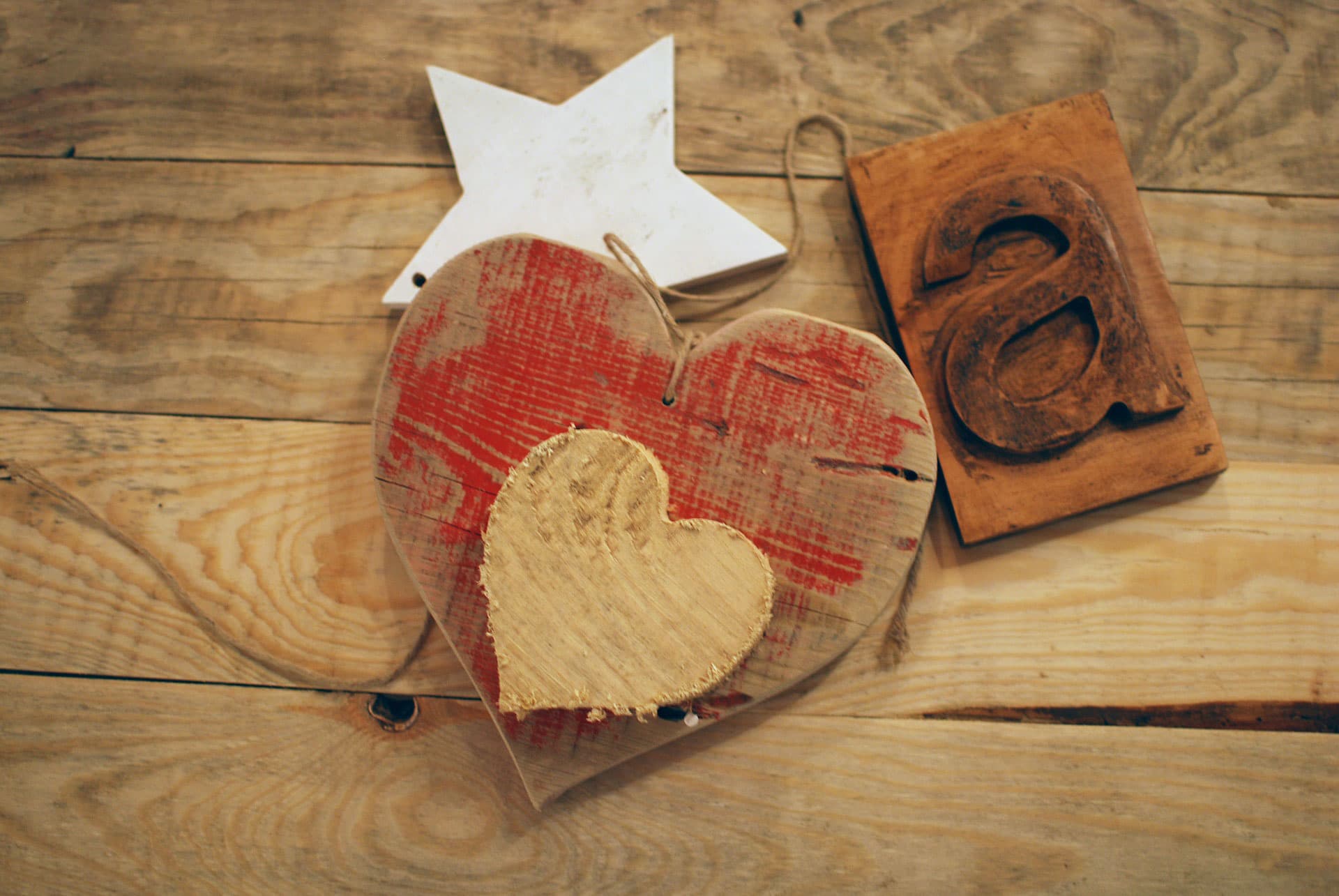 Wooden heart with red paint, smaller heart in center, a wooden star decoration, and a carved wooden letter a lying on a textured wooden surface.