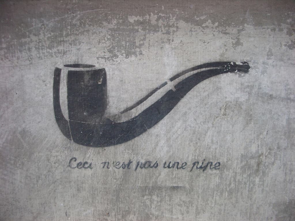 A black stencil drawing of a smoking pipe is centered on a rough, textured wall. Below the pipe, the text reads Ceci nest pas une pipe in a cursive font.