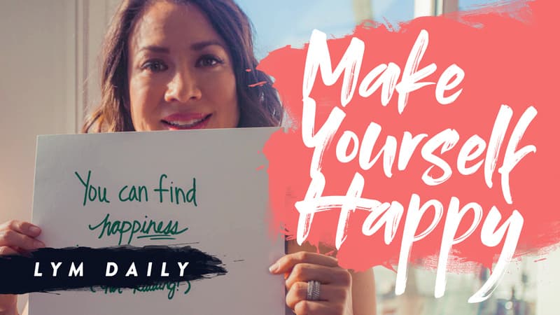 A person holds a sign reading You can find happiness (keep smiling), with large text next to them saying Make Yourself Happy on a pink background. The phrase LYM Daily is written on a black brushstroke.