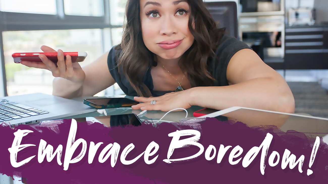 Woman sitting at a desk with a laptop and phone, looking frustrated. The text Embrace Boredom! is written in bold, playful font at the bottom of the image.