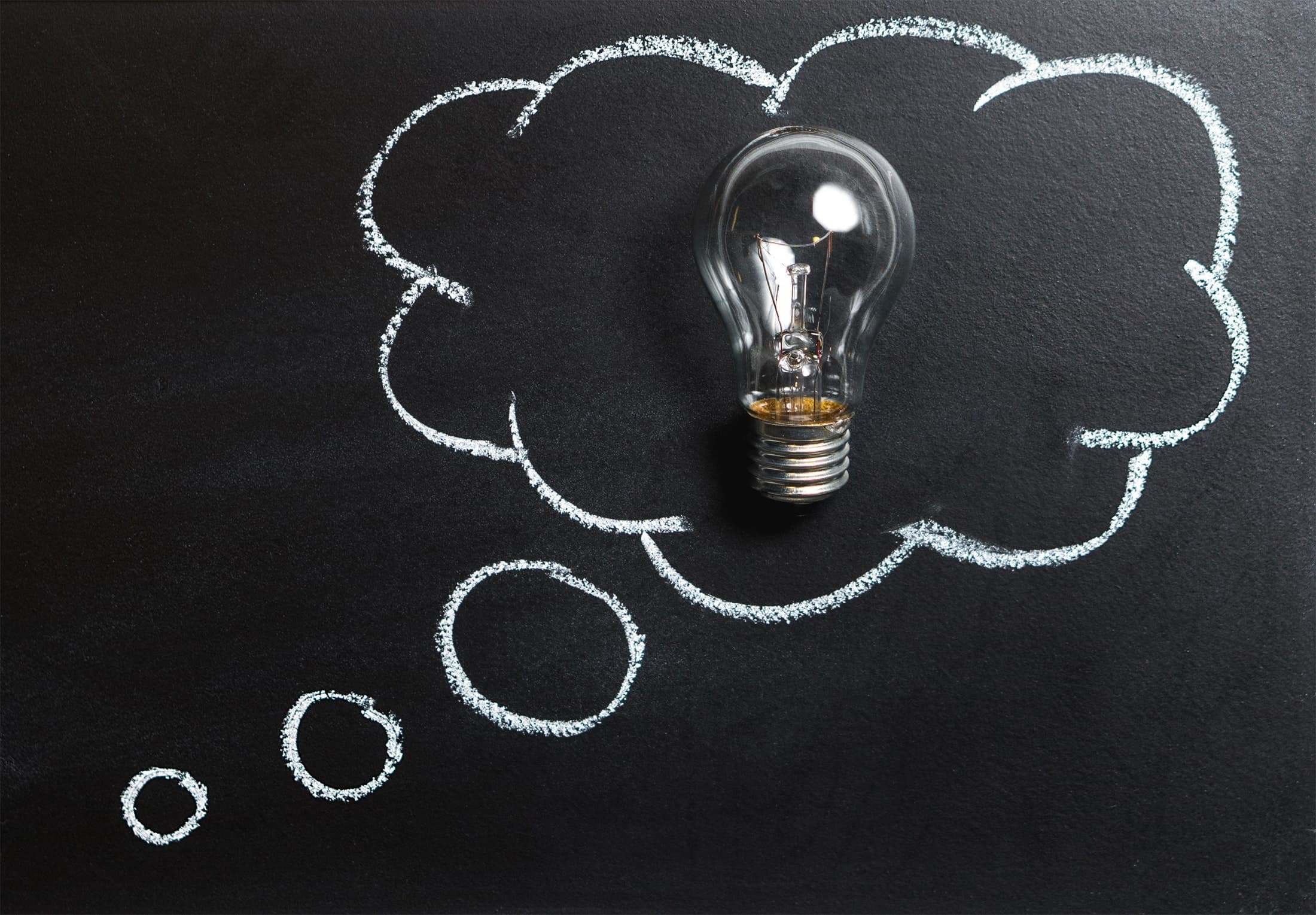 A light bulb is placed over a chalk drawing of a thought bubble on a blackboard, symbolizing creativity and new ideas.