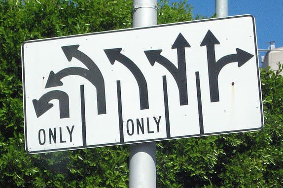 A street sign shows multiple black arrows with varied directions for lanes. Two middle lanes are labeled ONLY for straight or right turns, while the leftmost is for U-turns, and the rightmost is for going straight or turning left or right.
