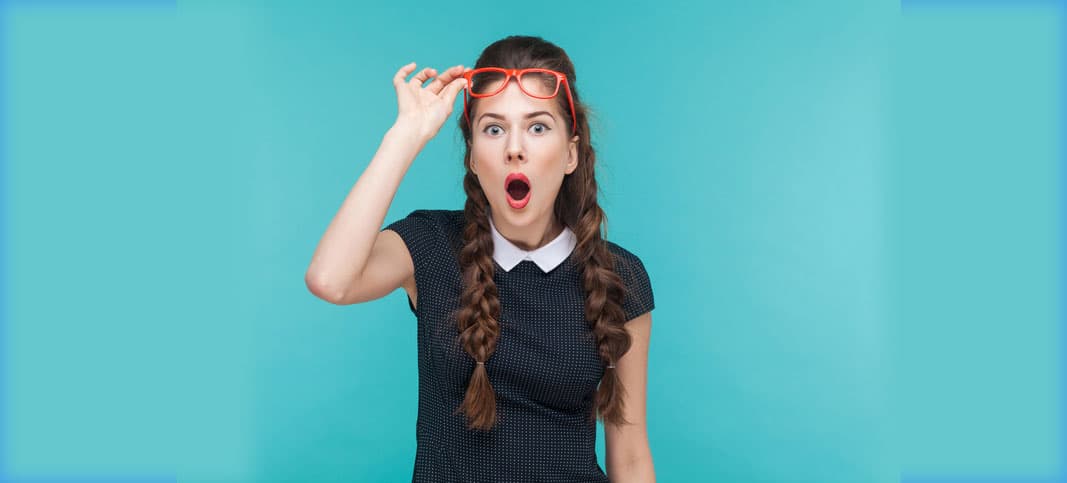 A woman with long brown braided hair and a black dress with a white collar looks surprised. She is adjusting her orange glasses while standing against a blue background.