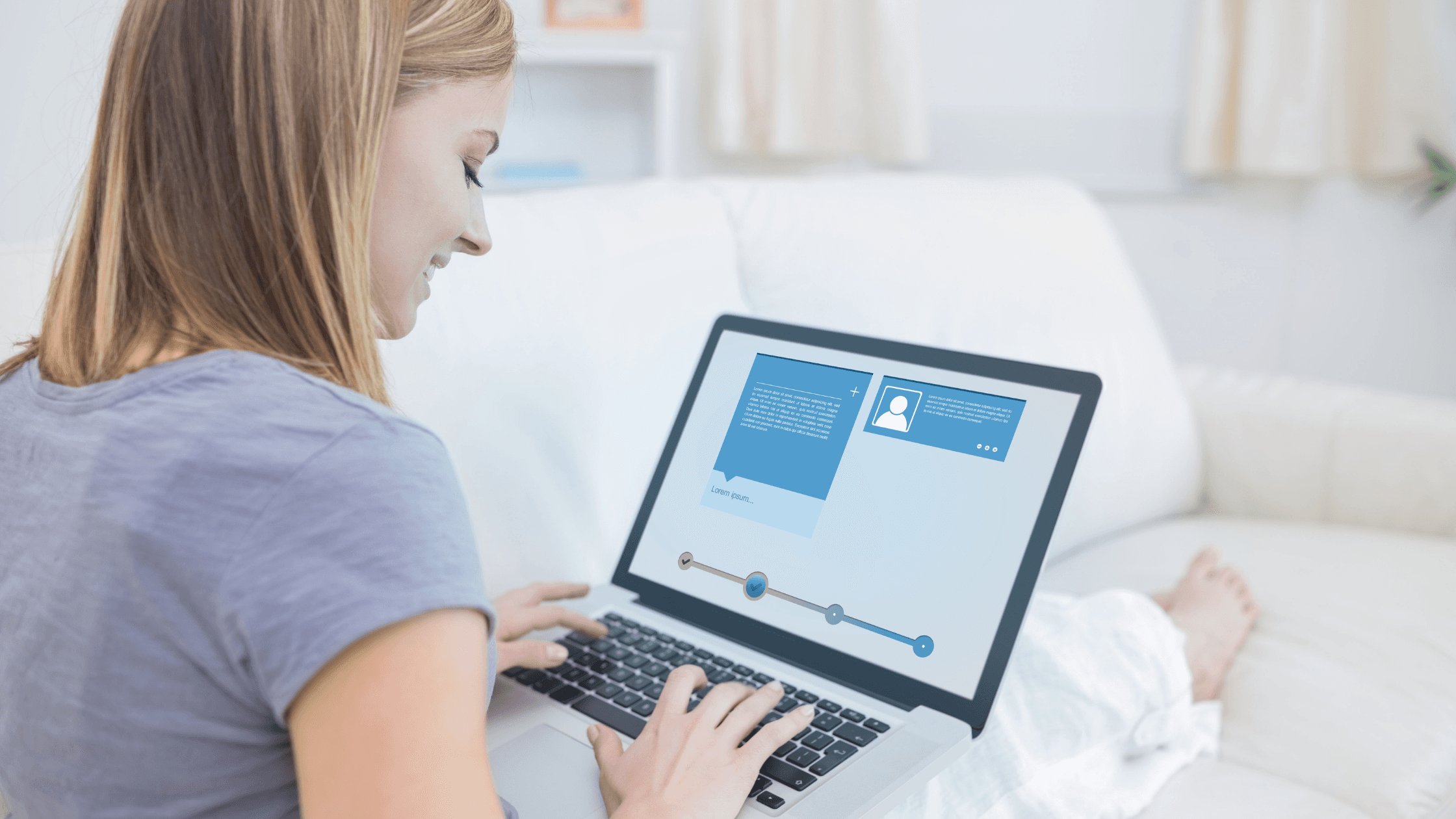 A woman sitting on a white couch uses a laptop with a blue and white interface displaying a social media profile. She is dressed casually in a light gray top and white pants. The room is bright, with soft natural lighting.