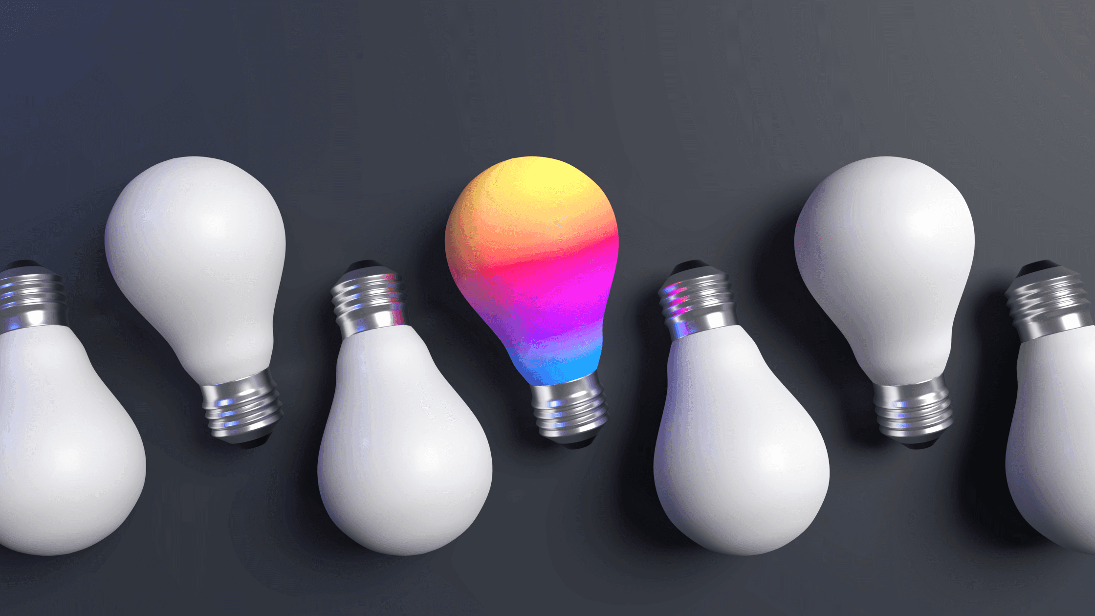 A row of white light bulbs is arranged on a dark surface, with one bulb in the center displaying a vibrant gradient of colors ranging from pink to yellow, standing out among the rest.