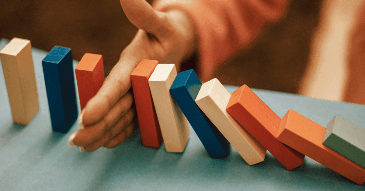 A hand stops a row of colorful wooden blocks from falling like dominoes.