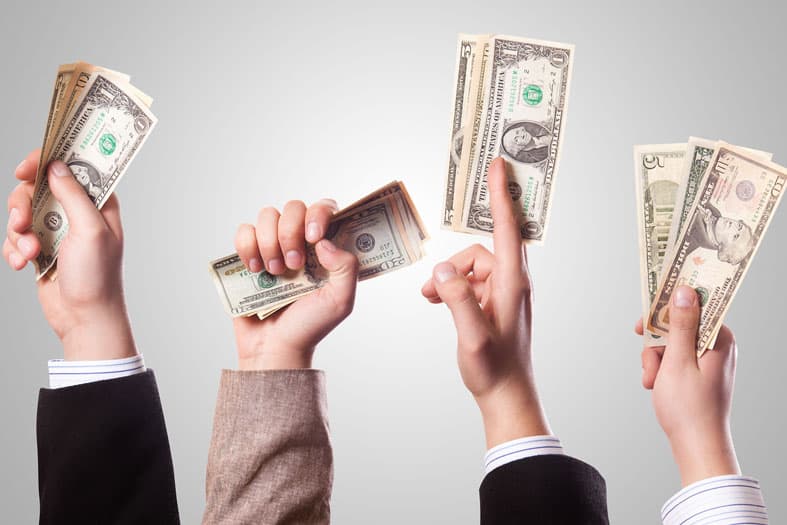 Three hands holding different amounts of U.S. dollar bills against a plain background, with each hand representing individuals in business attire, showcasing the concept of money and finance.