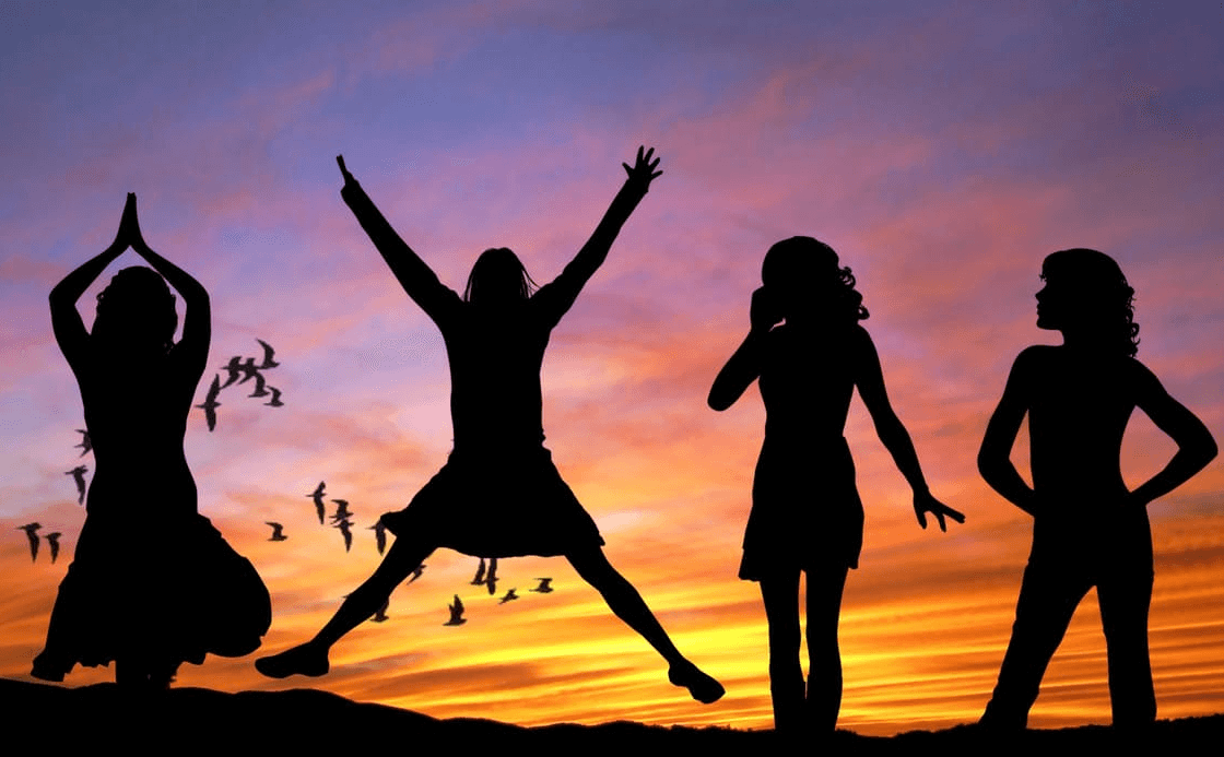 Silhouettes of four people against a vibrant sunset. One person stands with hands in prayer, another jumps with arms raised, while the remaining two strike different poses. Birds fly in the background, and colorful clouds fill the sky.