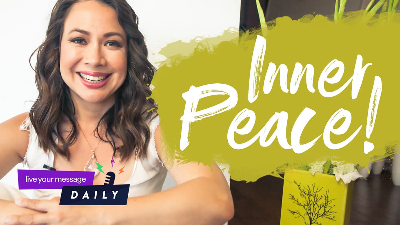 A woman with long brown hair smiles at the camera. She is seated with her arms on a table. A green sign next to her displays the text Inner Peace! with bright, bold letters. A live your message daily logo is in the lower-left corner.