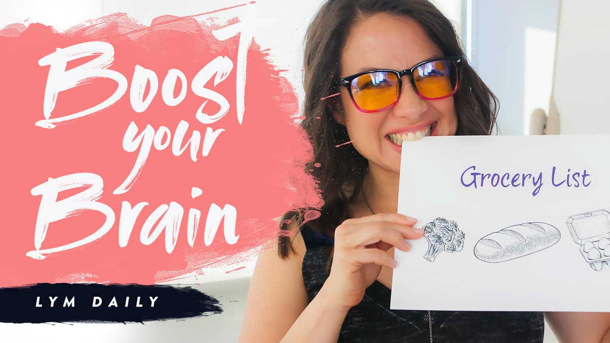 A person wearing glasses smiles and holds a drawing of a Grocery List with broccoli, bread, and eggs sketched on it. The background has the text Boost your Brain and LYM Daily in bold letters on a pink and white design.