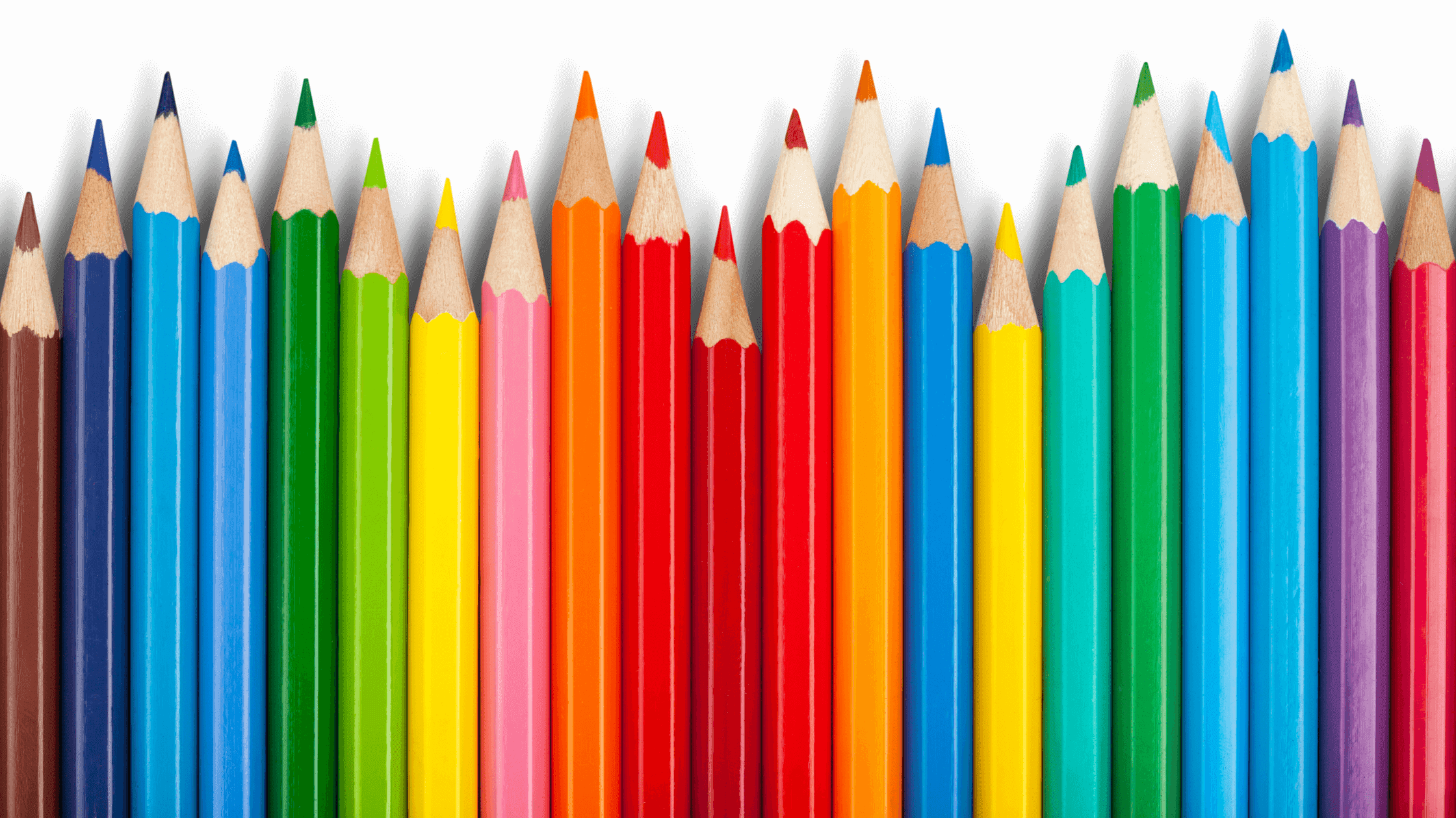 A row of colorful sharpened colored pencils arranged vertically. The pencils range in shades from dark brown to vibrant colors like green, pink, red, orange, blue, and yellow, set against a plain white background.
