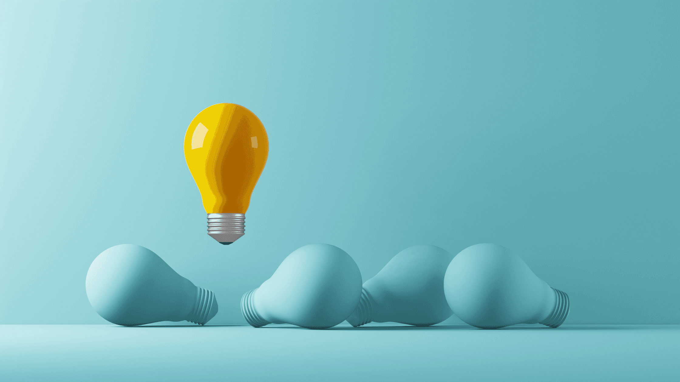 A bright yellow light bulb stands upright and lit against a blue background, symbolizing innovation. It contrasts with three unlit blue light bulbs lying down in the foreground, conveying ideas of creativity and uniqueness.