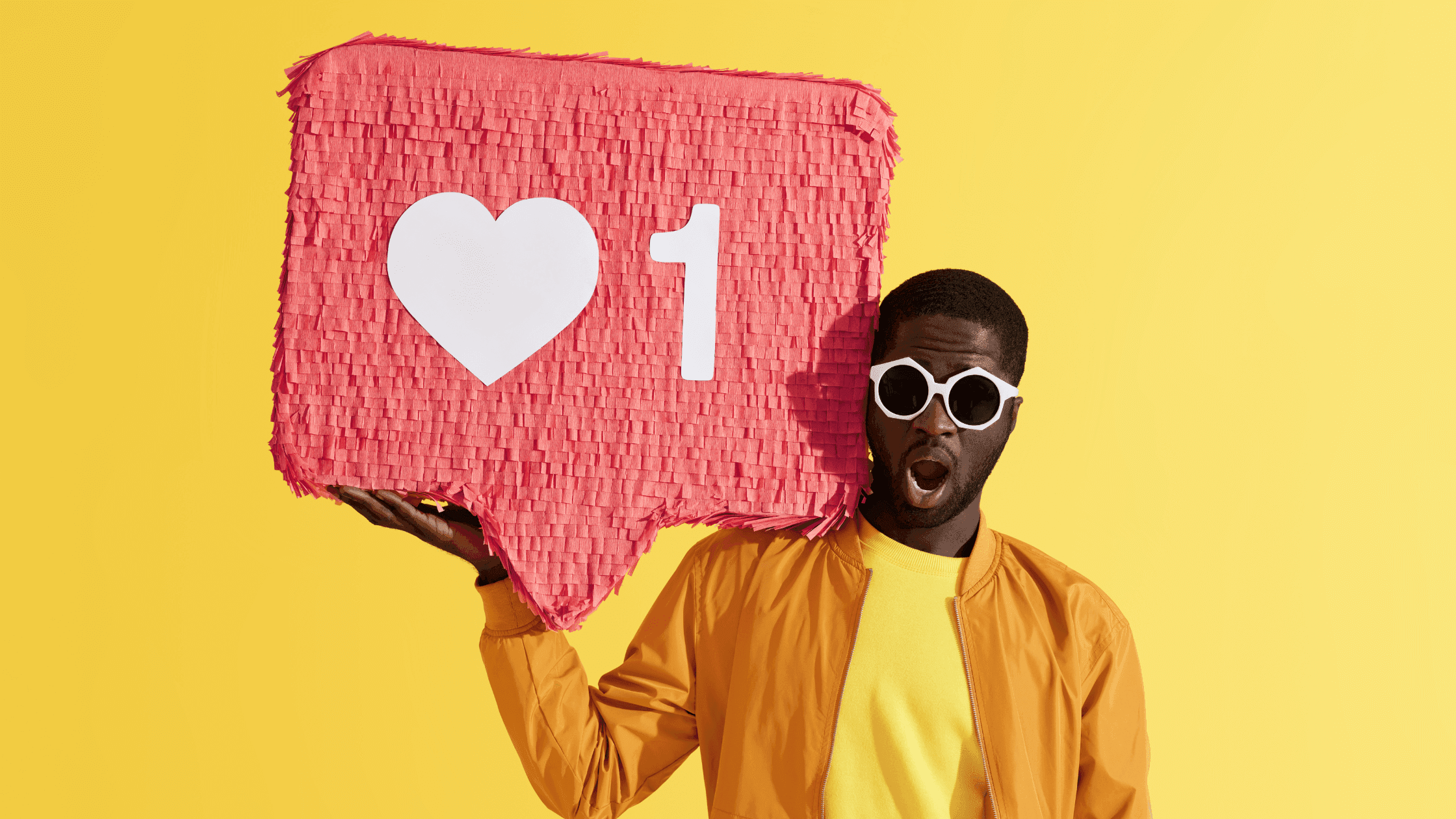 A person wearing sunglasses and a yellow jacket holds a large pink social media notification icon with a heart and the number one on a bright yellow background.
