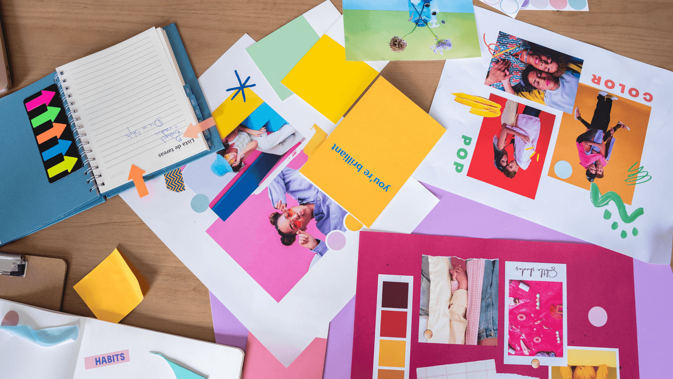 A colorful creative workspace with collage materials, including photos, color swatches, sticky notes, and an open notebook with tabs. The desk is cluttered with papers and art supplies, suggesting an ongoing design project or brainstorming session.